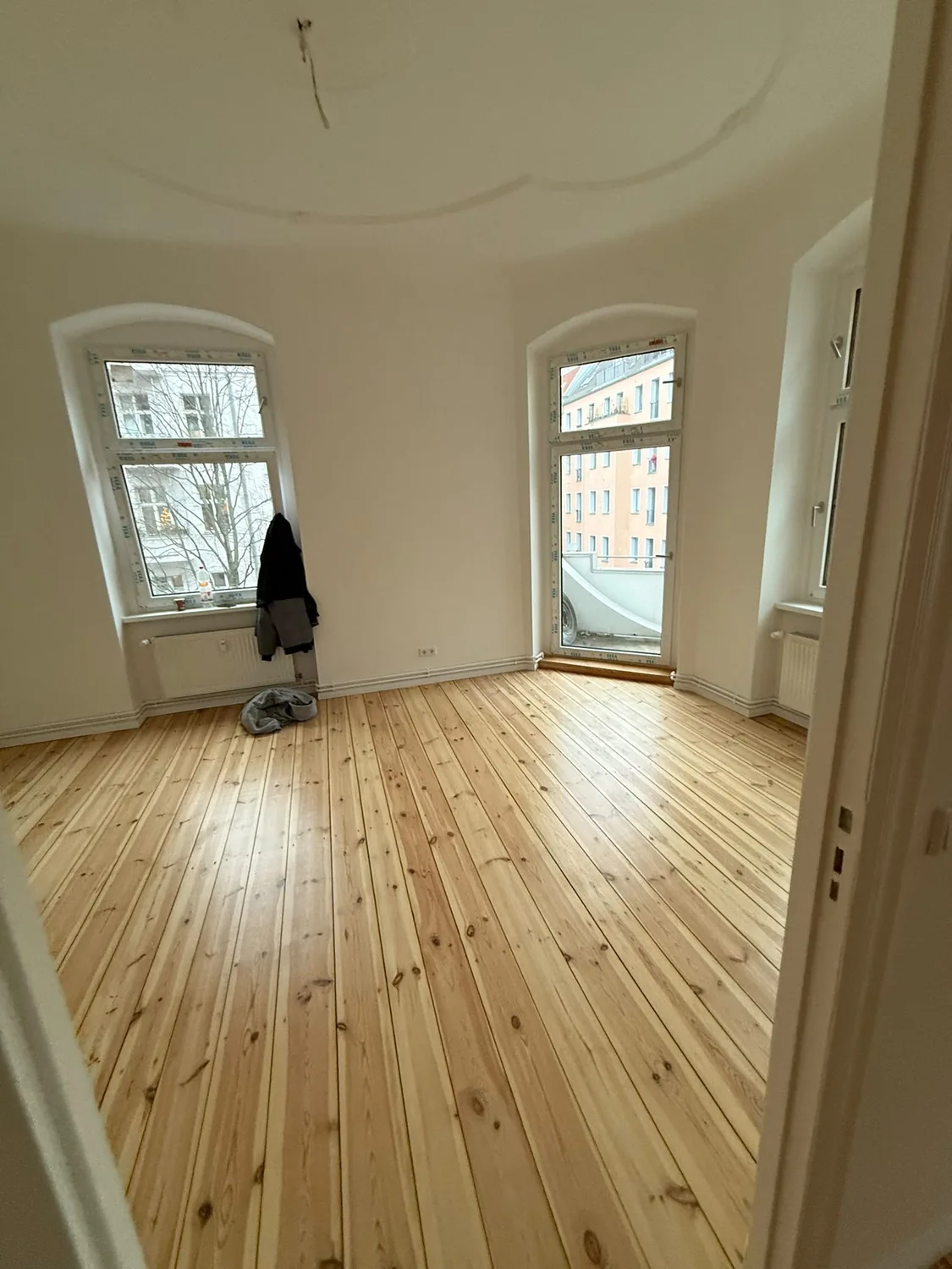 Altbau-Wohnraum vor und nach der Renovierung mit denselben beiden Fenstern und der Balkontür – Nachher